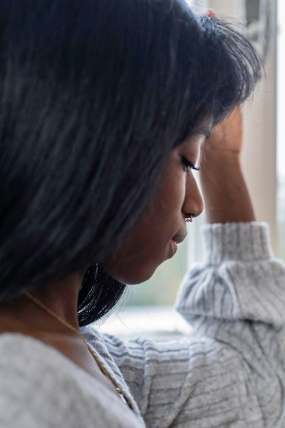 Eenzame jonge Afrikaanse vrouw die thuis voor het raam naar beneden kijkt Depressief zwart meisje met droevige uitdrukking