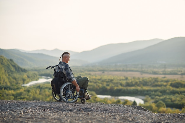 Eenzame jonge man in een rolstoel genieten van frisse lucht in zonnige dag op de berg