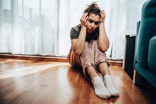 Eenzame jonge vrouw in depressie zit bij het raam verloren in slechte pessimistische gedachten.