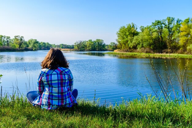 Eenzame jonge vrouw zittend op een oever van de rivier