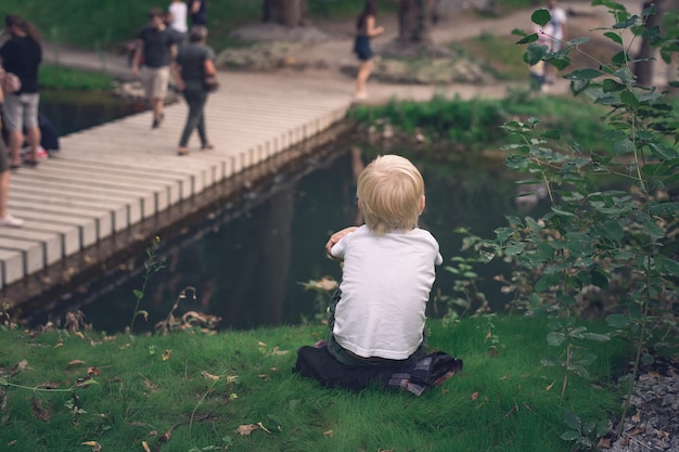 Eenzame jongen in het park Kind zit op gras en kijkt naar mensen Achteraanzicht