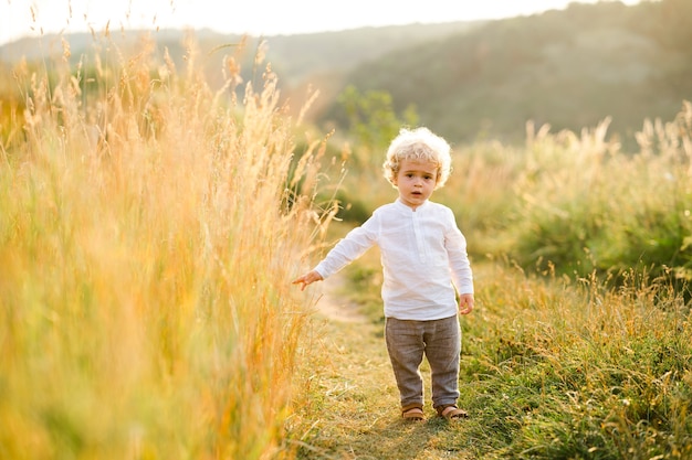 Eenzame jongen met krullend haar en blond haar loopt over het veld