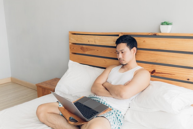 Eenzame man werkt met zijn laptop op zijn gezellige bed. Concept van freelancer werk levensstijl.