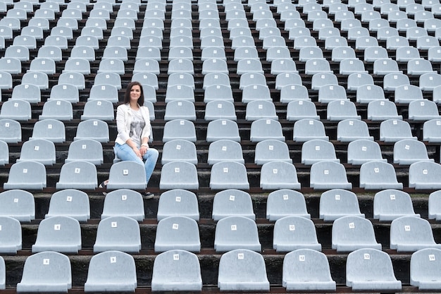 Eenzame mooie vrouw zittend op een grijze lege stadion tribunes in de regen