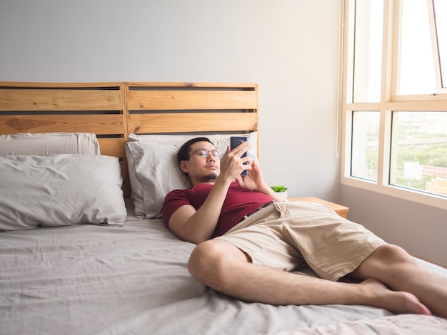 Eenzame niet-sociale Aziatische man met zijn smartphone in zijn slaapkamer appartement.