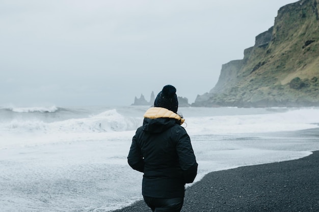 Eenzame vrouw in regenkleding op het zwarte zandstrand in Vik i Myrdal in IJsland tijdens een humeurige dag vol water Beleef je droomliefde in roadtripstijl in IJsland Bezoek IJslandCopy space image