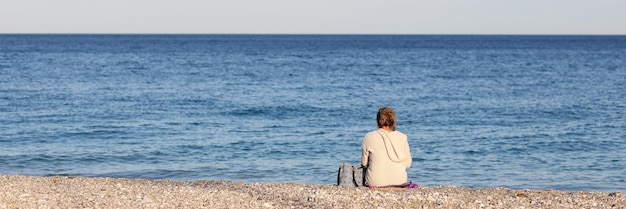 Eenzame vrouw zit met rug en kijkt naar zee lopend op zee verdriet en verwachtingsconcept