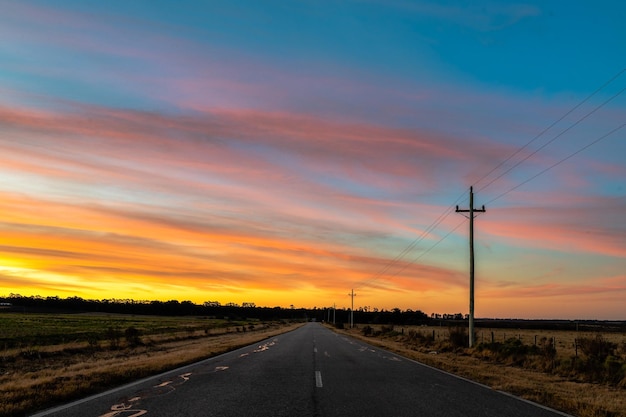 Eenzame weg door het landschap met een hoogspanningslijn aan de rechterkant onder tijdens zonsondergang