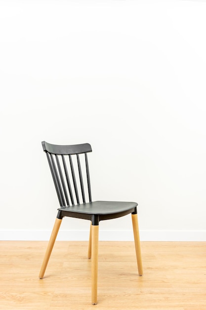 Eenzame zwarte stoel met kleurloos gelakte beukenhouten poten in witte kamer met eikenkleurige vloer
