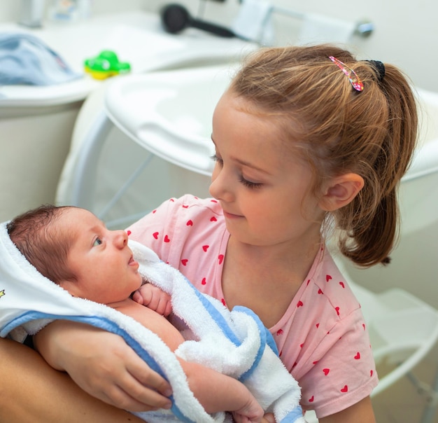 Eerste badje pasgeboren jongetje De baby ligt in de badjas in de armen van zijn zusje