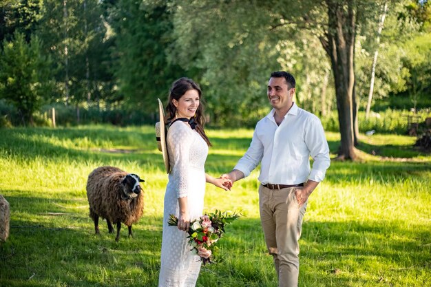 Eerste huwelijksdans van jonggehuwd jong mooi paar verliefd in trouwjurken staande op een groen weidevee op de achtergrond