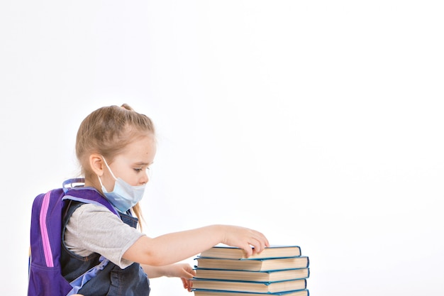 eerste-klasser leert lezen. een klein meisje op afstandsonderwijs thuis. kind in een medisch masker leest een boek.