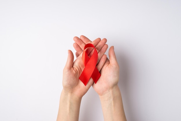 Eerste persoon bovenaanzicht foto van vrouwelijke handen met rood zijden lint in gekruiste palmen symbool van aids bewustzijn op geïsoleerde witte achtergrond