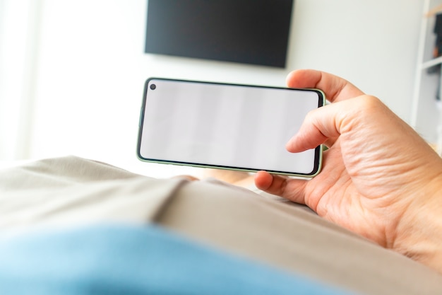 Eerste persoonsmening van de mens die smartphone gebruikt terwijl hij op het bed ligt.