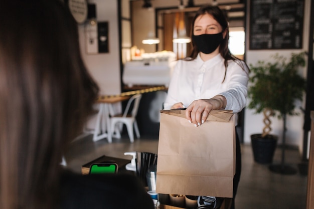 Eerste persoonsmening van klant nemen pakket met koffie en eten van kassier in masker bij café nemen