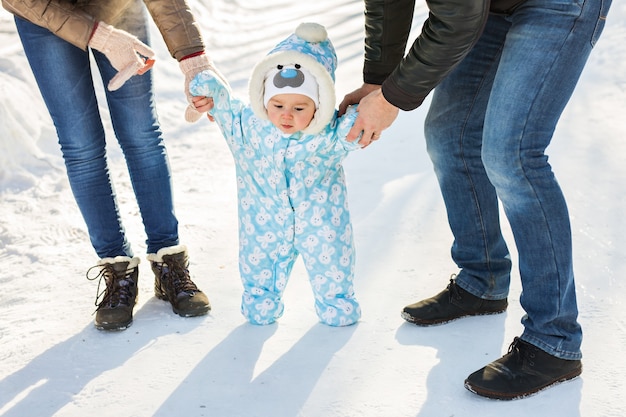 Eerste stappen. Kleine baby die leert lopen. Moeder en vader met peuterjongen in het winterpark