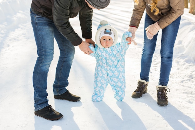 Eerste stappen. Kleine baby die leert lopen. Moeder en vader met peuterjongen in het winterpark