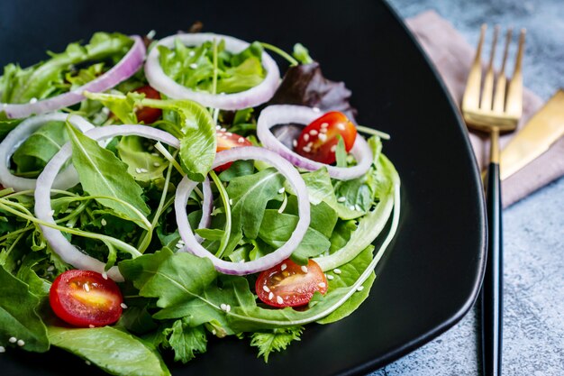 Eet groen concept met organische verse groentesalade in ceramische plaat op zwarte achtergrond.