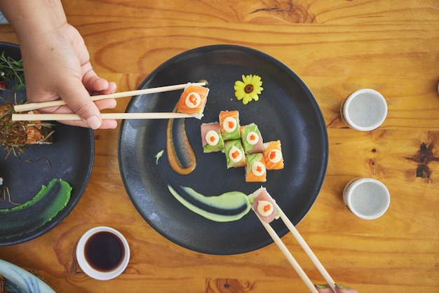 Eetstokjes hand en sushi en eten eten in een restaurant voor voeding aan tafel Boven hongerige mensen met houten stokken en sojasaus om te dineren Japanse cultuur en keuken met kunst op een bord