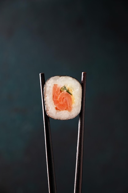 Eetstokjes houden een sushi-broodje met zalm close-up op een donkere achtergrond Concept Japans eten