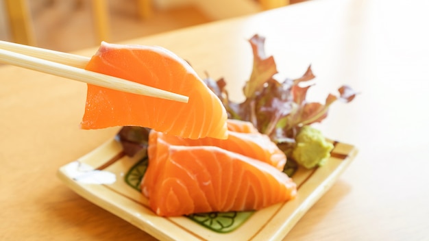 Eetstokjes tong verse zalm sashimi op een houten tafel