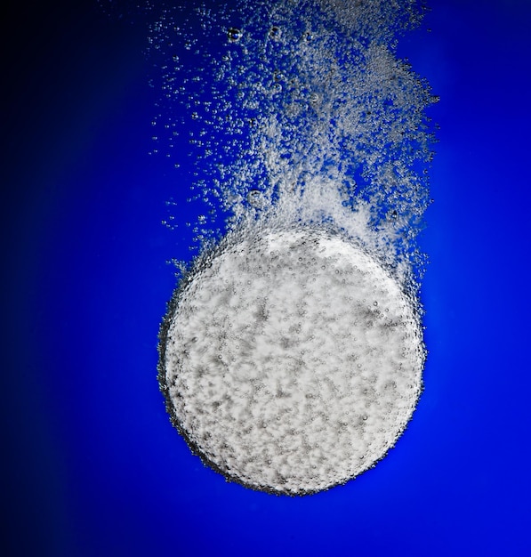 Effervescent tablet in water with bubbles on a blue background