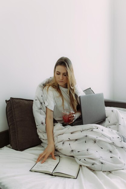 Foto una giovane ragazza millenaria efficiente seduta su un letto la mattina usa la foto del computer portatile con