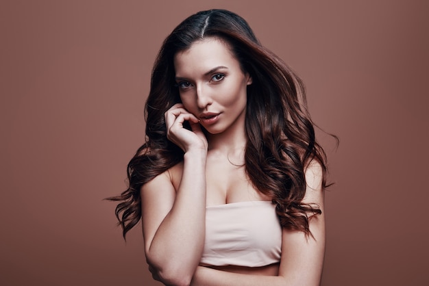 Effortless beauty. Attractive young woman looking at camera while standing against grey background