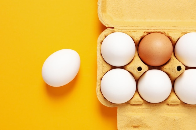 Egg box with eggs on orange background top view