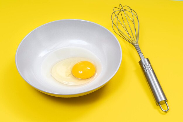 An egg in the dish with a beater on a yellow surface