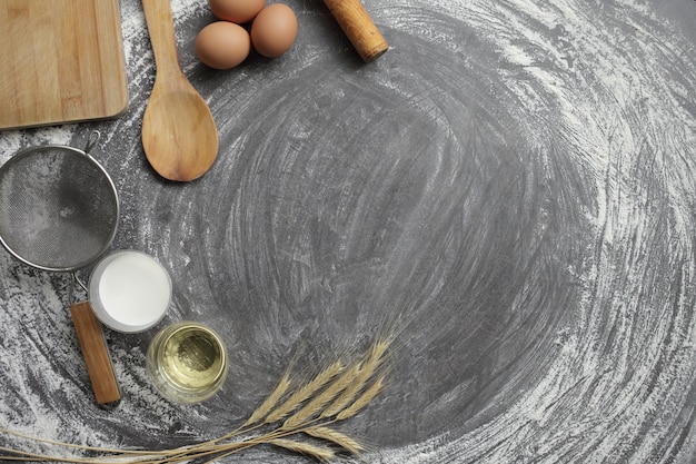 卵、小麦粉、オリーブオイル、牛乳、小麦の穂、灰色のテーブル背景にキッチンツール。