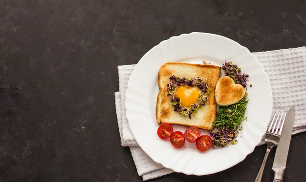 Egg in a hole of bread heart shape, microgreens, healthy food
breakfast, tea, black background