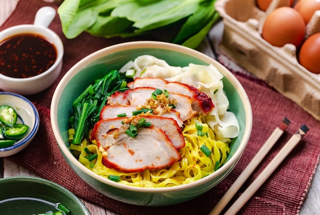 Photo egg noodle with barbecued red pork serving with local sweet sauce and white sesame and green chili in vinegar