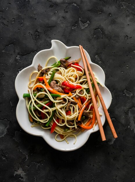 egg noodles with wok vegetables green beans sweet peppers carrots onions in a bowl on a dark background top view