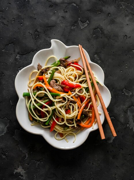 Egg noodles with wok vegetables green beans sweet peppers carrots onions in a bowl on a dark background top view