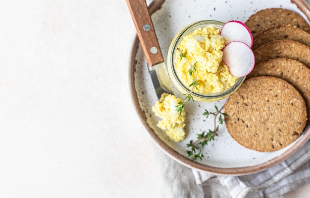 Egg pate salad or dip in glass jar served with radish thyme and multigrain crackers