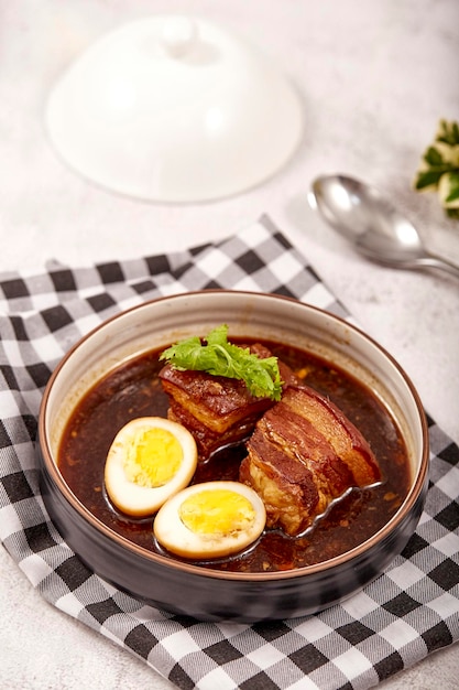 Egg and Pork in Sweet Brown Sauce in bowl placed on tablecloth 2 boiled eggs braised pork and cilantro popular food in asia