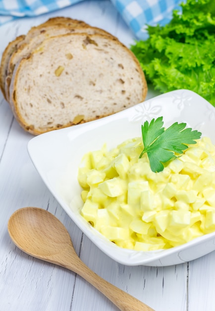 Egg salad in a bowl with bread and lettuce on background