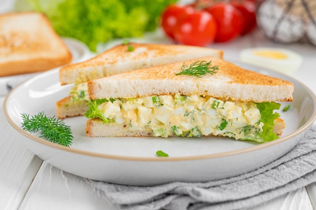 흰색 나무 배경에 구운 빵과 양상추를 곁들인 계란 샐러드 샌드위치