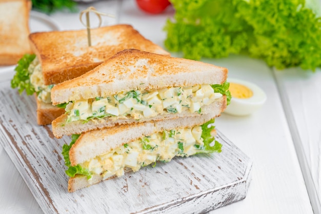 Panino con insalata di uova con pane tostato e lattuga su fondo di legno bianco messa a fuoco selettiva