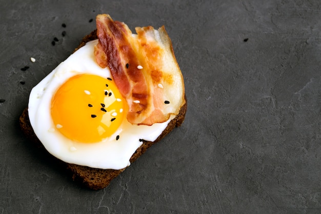 Egg sandwich and fried bacon on grey background.