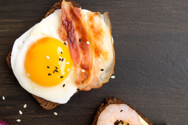 Egg sandwich and fried bacon on wooden background.