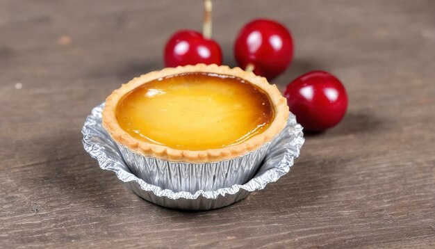 egg tart in aluminum foil cup with red cherry on wood table