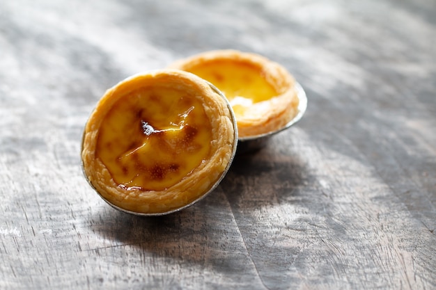 Egg tarts in aluminum foil cup on wood table,  traditional Portuguese dessert served in coffee shop