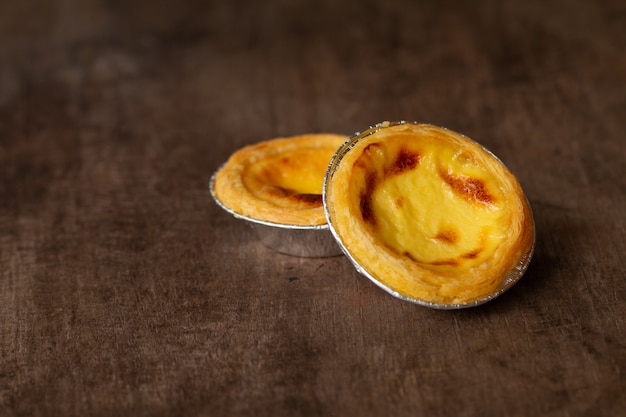 Egg tarts in aluminum foil cup on wood table,  traditional Portuguese dessert served in coffee shop