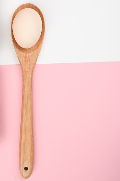 Uovo su un cucchiaio di legno. un vassoio di uova su uno sfondo bianco e rosa. vassoio eco con testicoli. tendenza minimalista, vista dall'alto. vassoio per uova. concetto di pasqua.