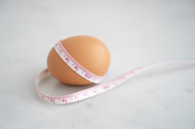 Egg wrapped with measure tape on white marble surface