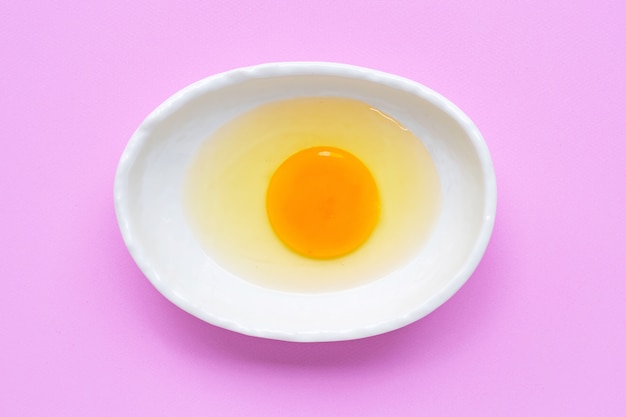 Egg yolk and white in a bowl on pink 