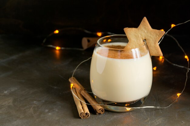 Eggnog cocktail and star cookies on black background.