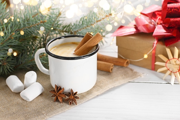 Eggnog with cinnamon anise and nutmeg in mug on  wooden table near the branches of a Christmas tree